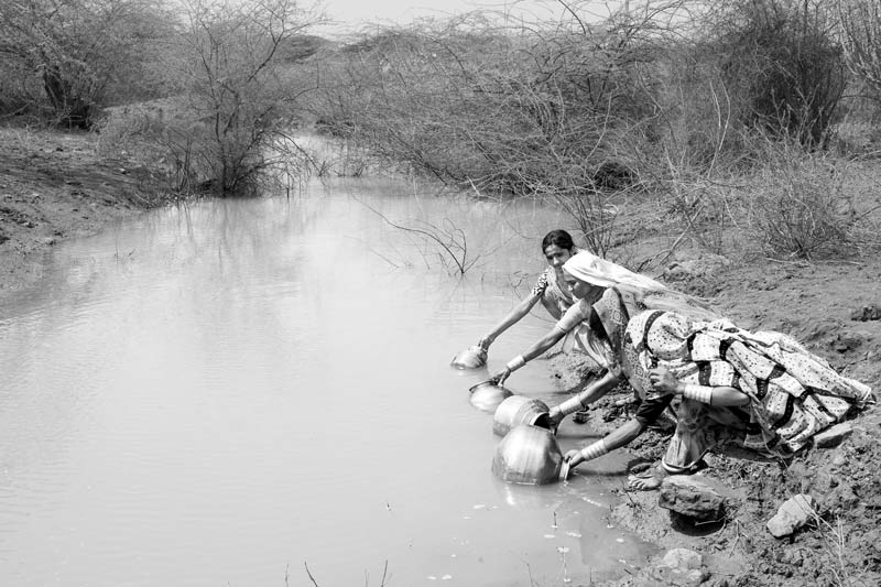 Rural Drinking Water Challenges - Women filling pitchers with drinking water at a distant shallow pond near agricultural fields in Kutch district, Gujarat